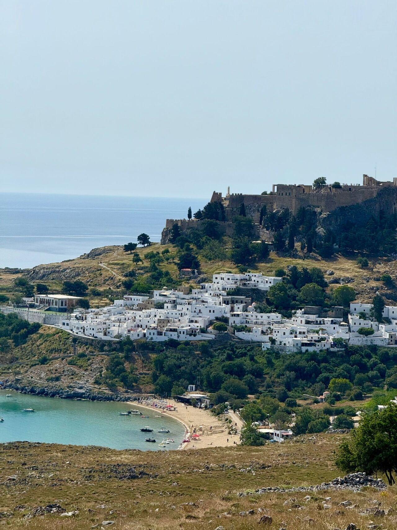 Weiß getünchte Häuser an der Küste mit Burg, Strand und türkisfarbenem Meer im Hintergrund.