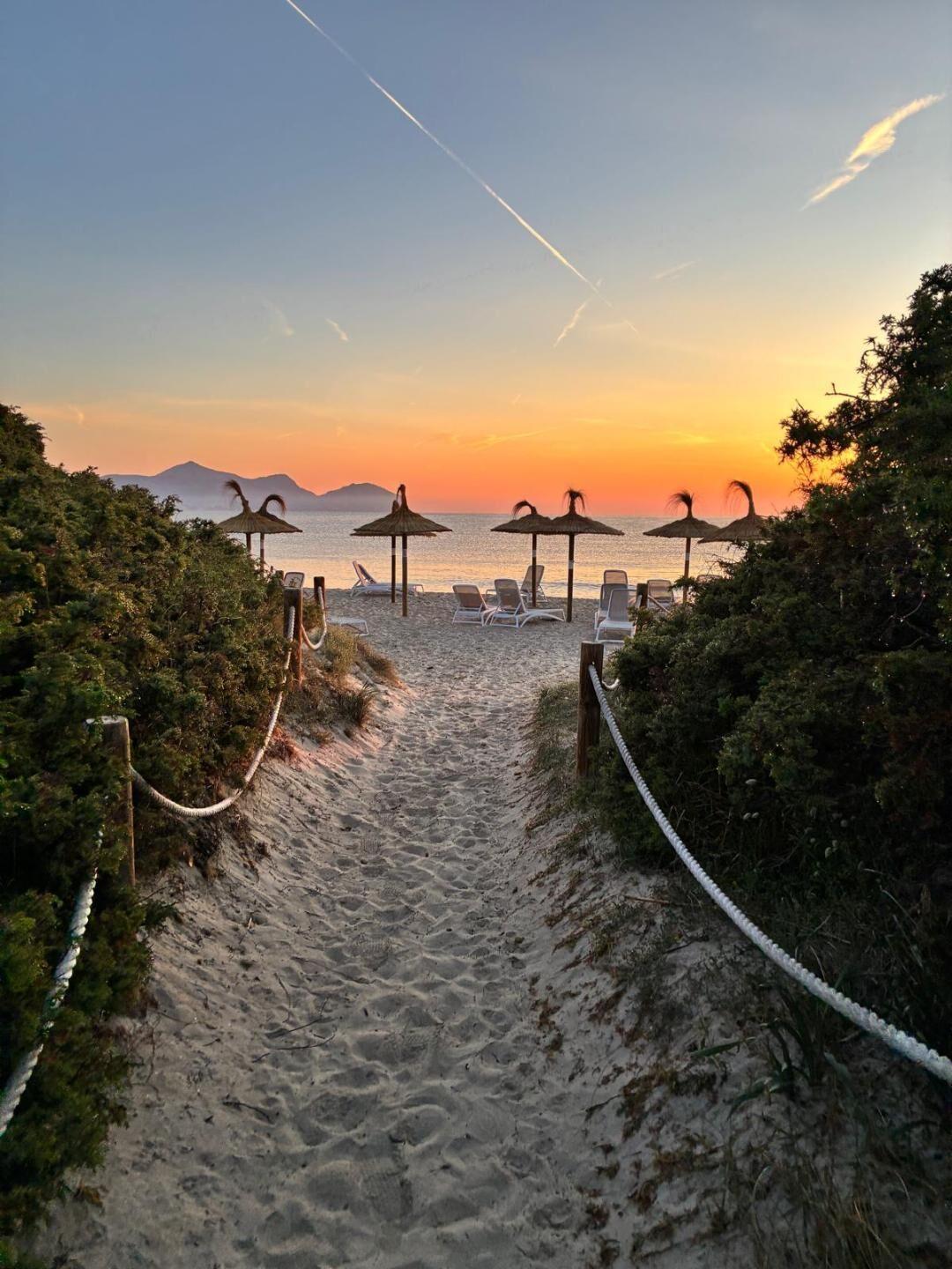 Sandiger Pfad führt zu leeren Liegestühlen und Strohhut-Sonnenschirmen am ruhigen Strand bei Sonnenuntergang.