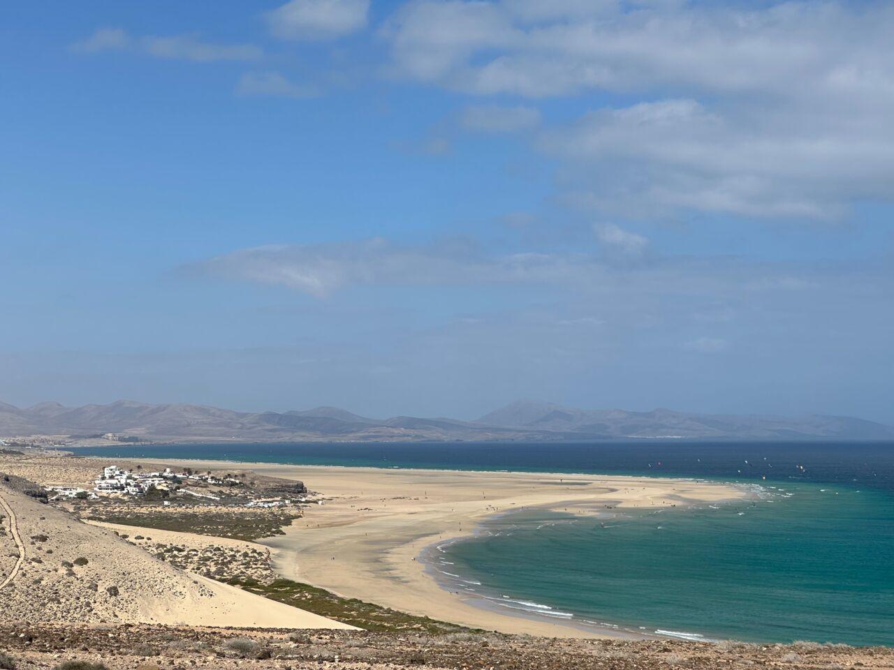 Weite Sandstrände treffen auf türkisblaues Meer unter leicht bewölktem Himmel an einem Küstenurlaubsort.