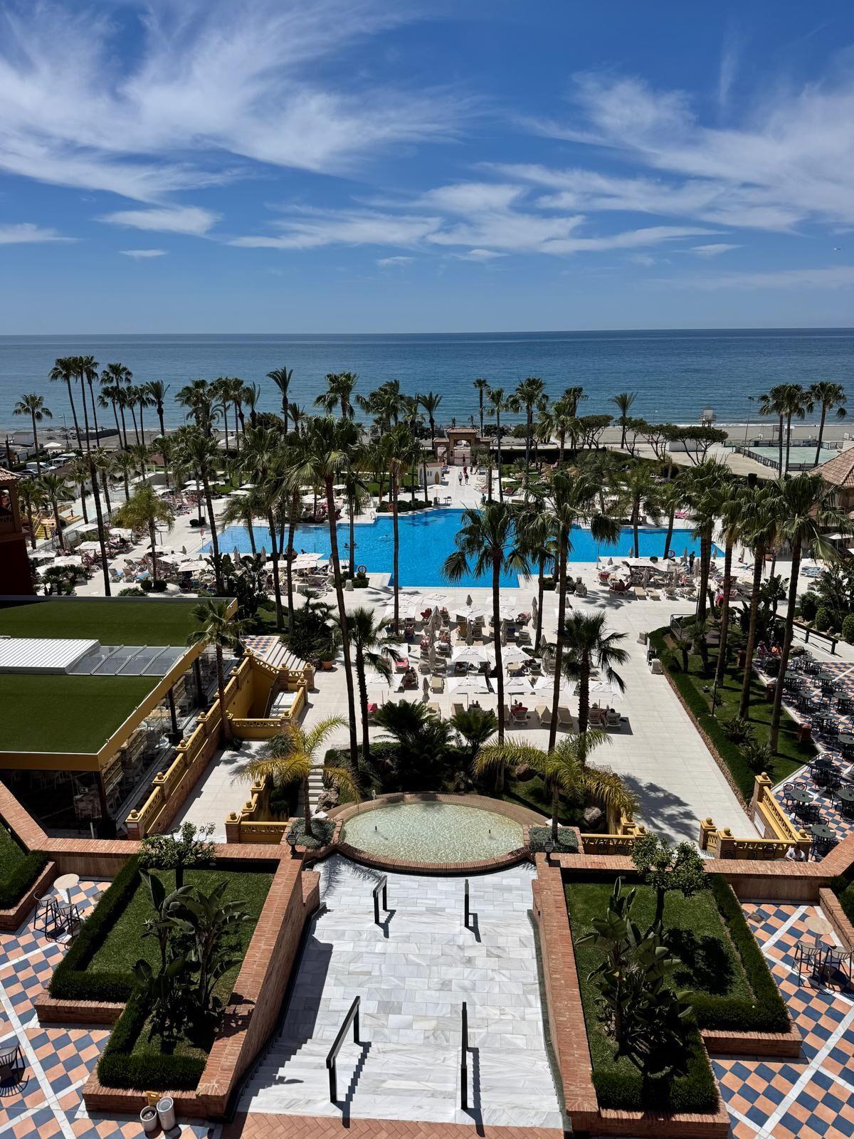 Hotel mit großem Pool, Palmen und Blick auf den blauen Ozean unter blauem Himmel.