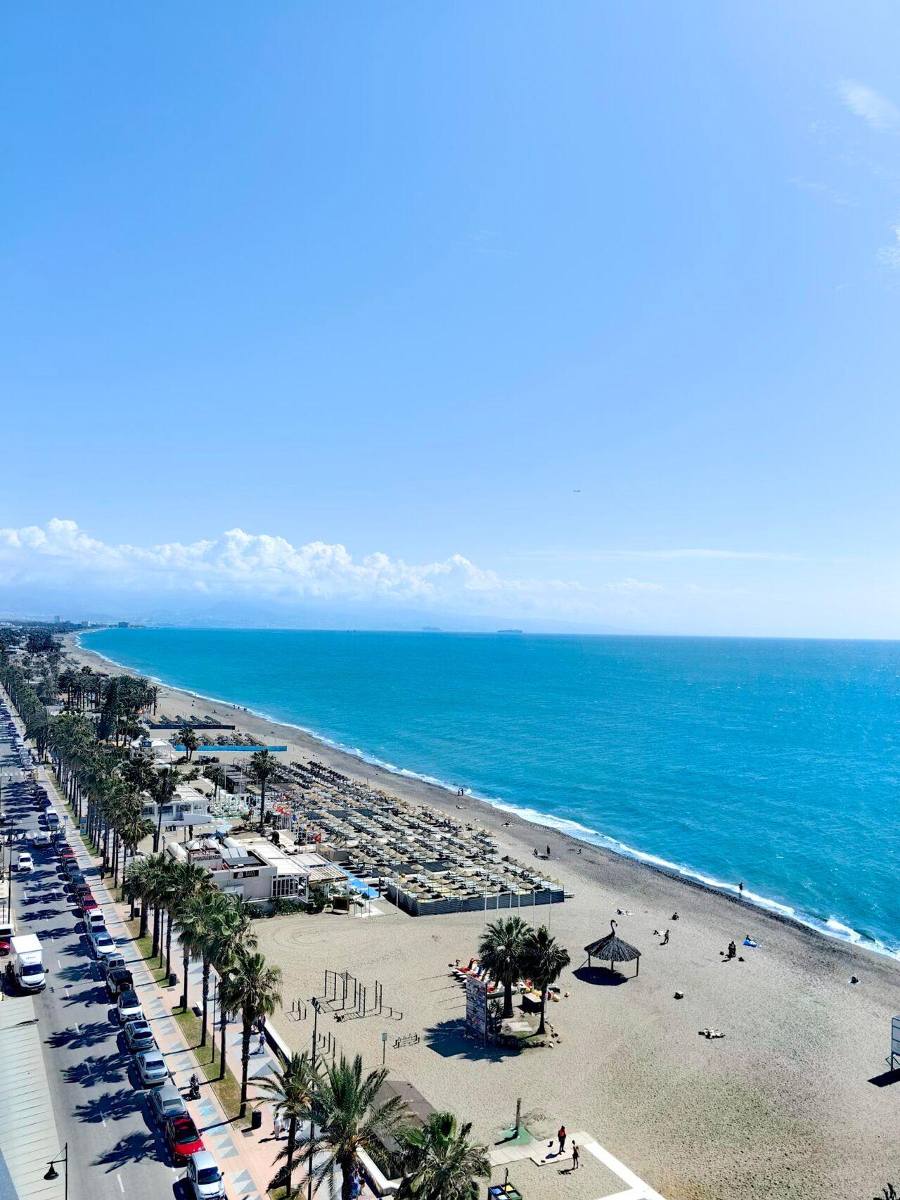 Weite Küste mit goldfarbenem Sand, blauem Meer, Strandliegen und Palmenlandschaft am Hotelboulevard.