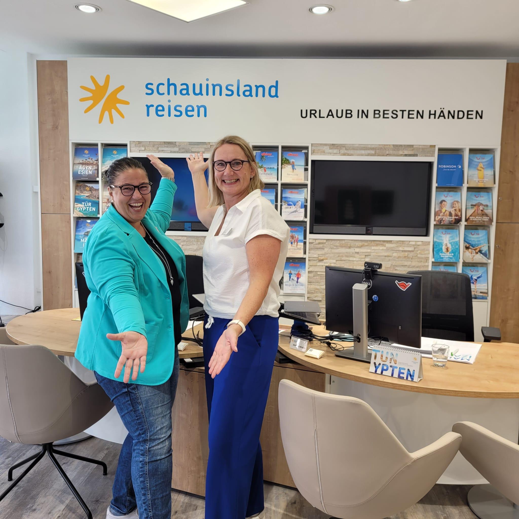 Zwei Frauen begrüßen in einem modernen Reisebüro von Schauinsland Reisen mit hellen Farben und Broschüren.