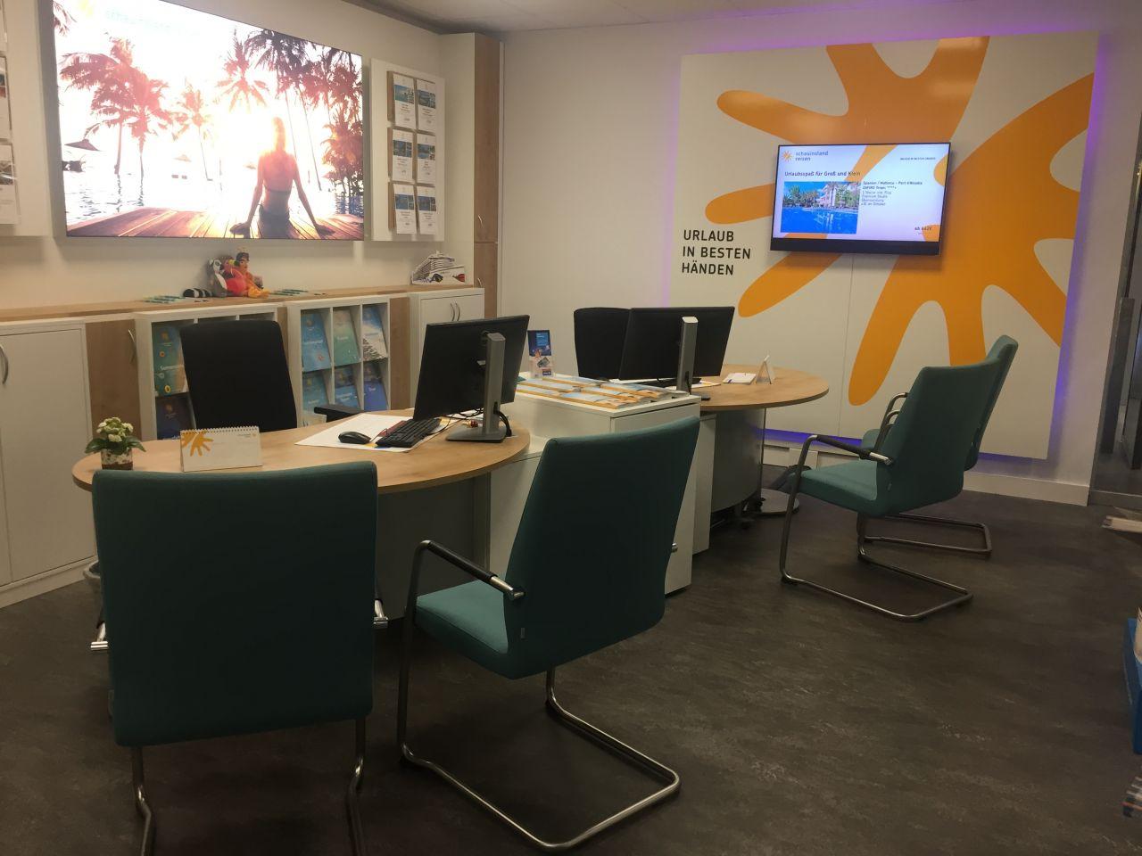 Moderne Reiseberatung mit Schreibtischen, grünen Stühlen und bunten Wanddekorationen in einem Büro.