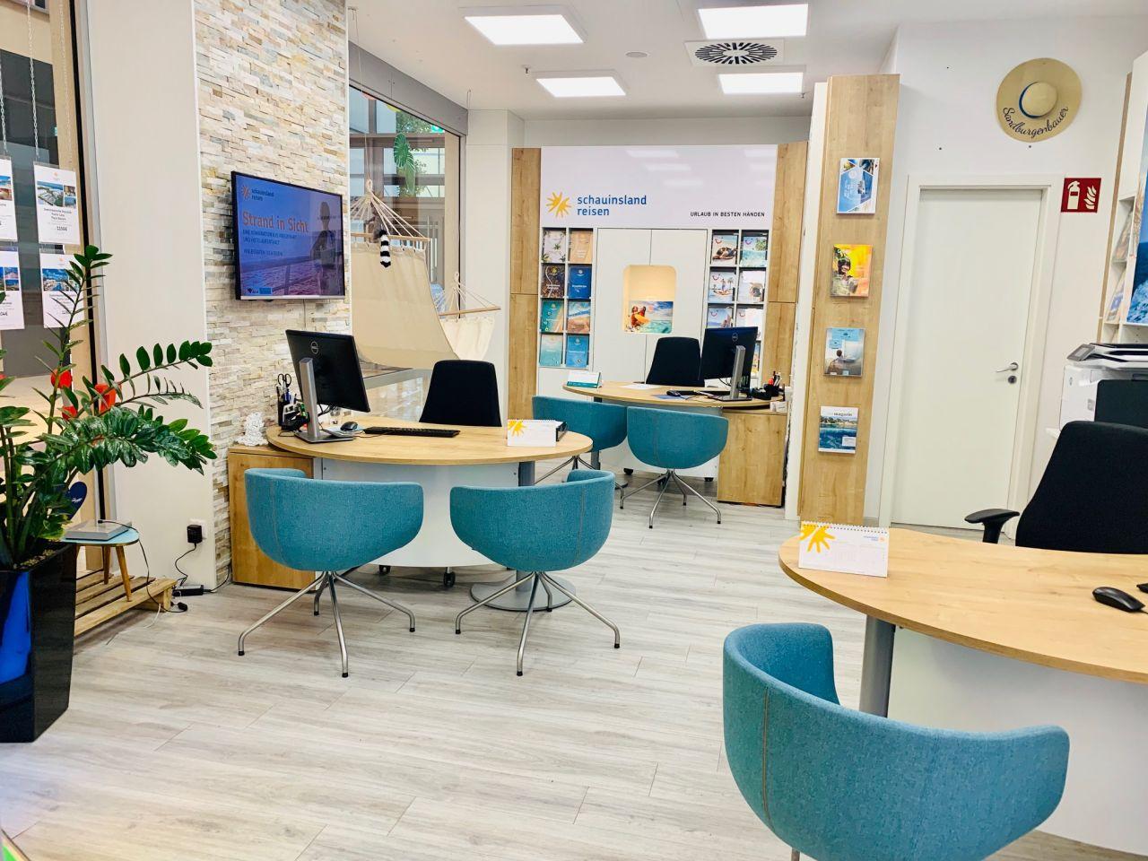 Modernes Reisebüro mit hellen Holzmöbeln, blauen Sesseln und Informationsmaterialien an den Wänden.