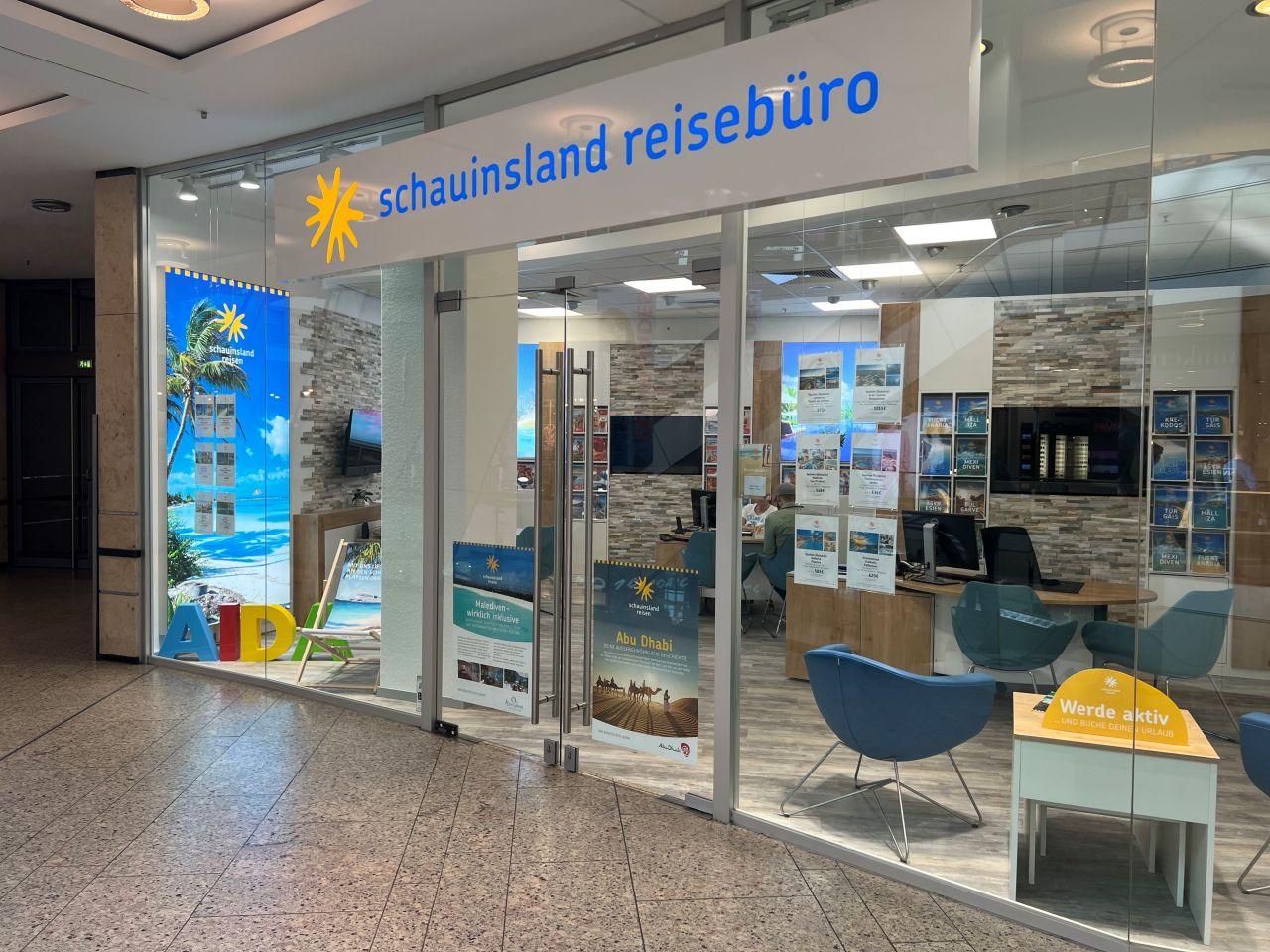 Ein modernes Reisebüro mit Glasfront, bequemen Stühlen und Urlaubsbildern am Strand.