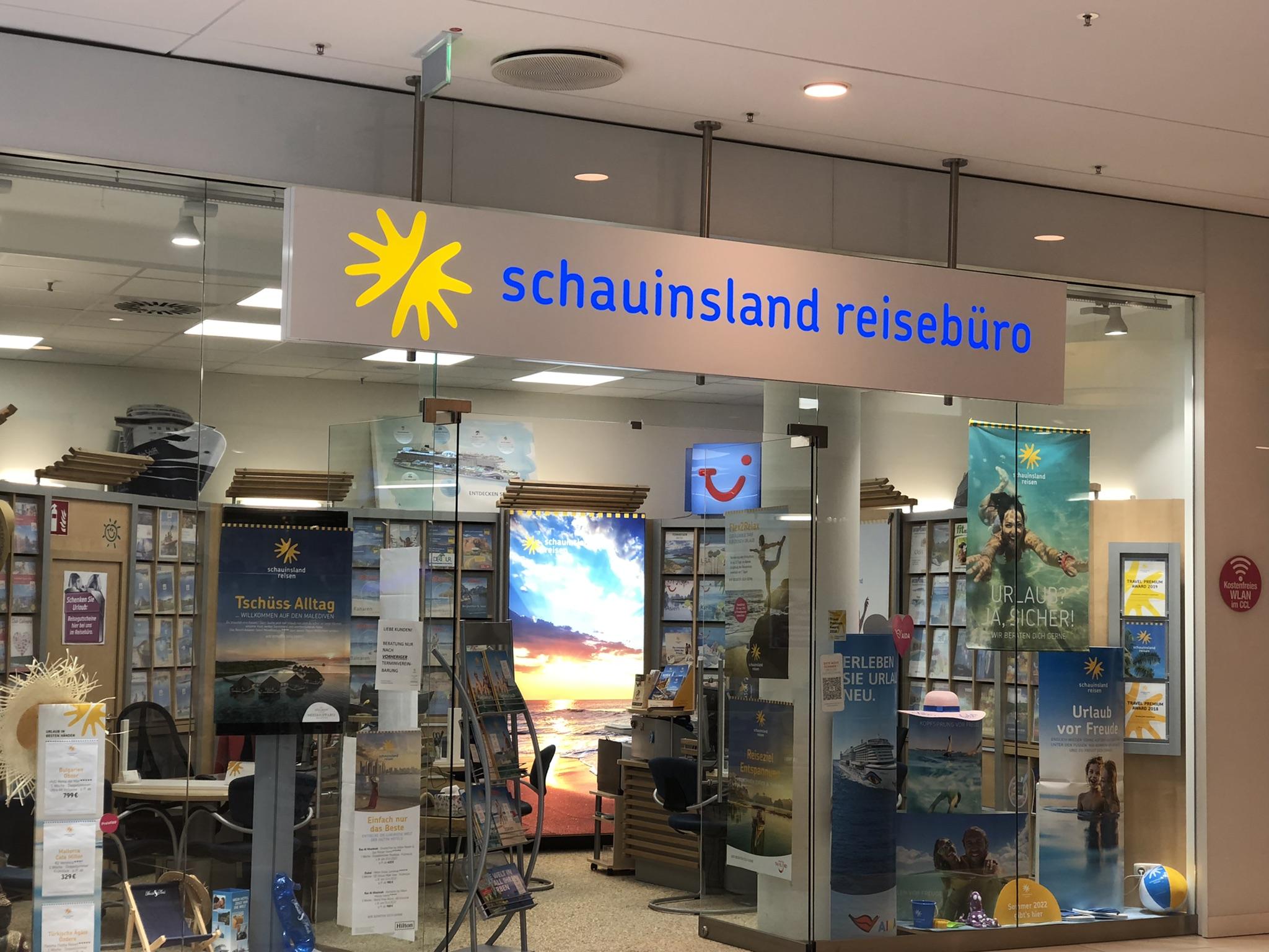 Modernes Reisebüro mit hellblauem Logo und zahlreichen Urlaubsmotiven und Broschüren im Schaufenster.