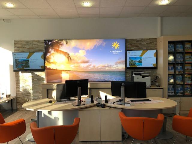 Moderner Reisebüro-Empfang mit Bild eines Sonnenuntergangs am Strand und orangefarbenen Stühlen.