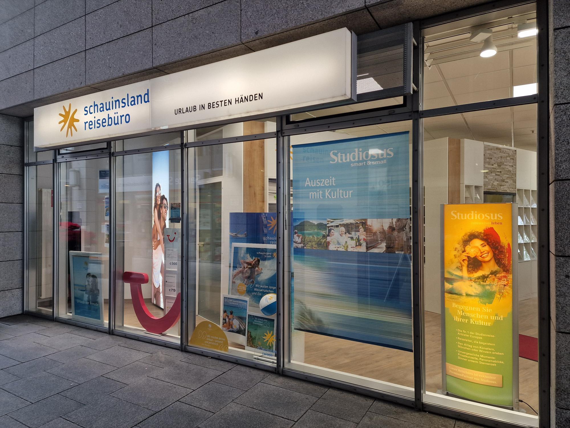 Modernes Reisebüro mit großen Glasfronten, hellen Werbebannern und Urlaubsmotiven an der Fassade.