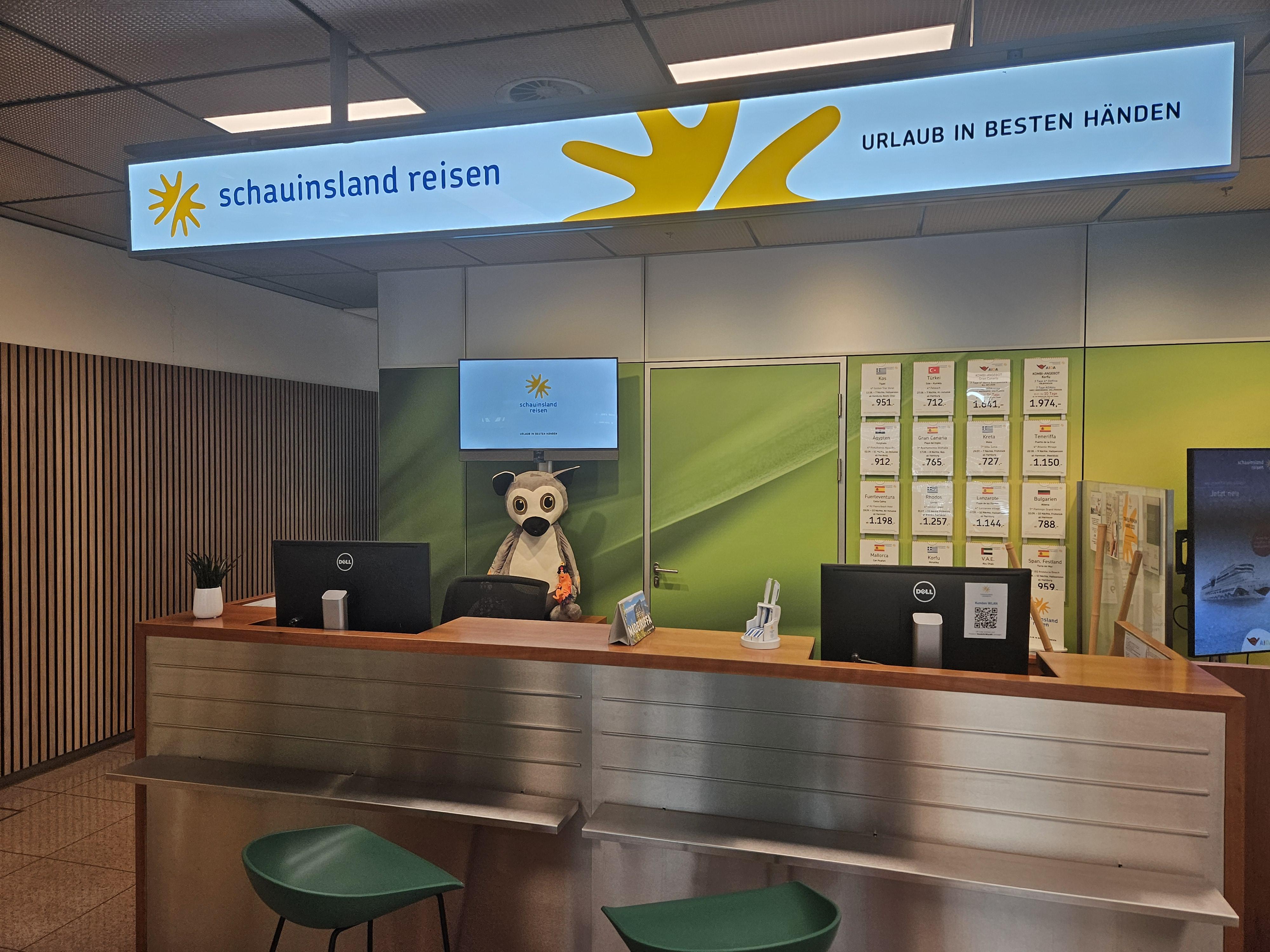 Reisebüro mit Empfangstresen, grüner Wand und Maskottchen im Büro für Urlaubsplanung.