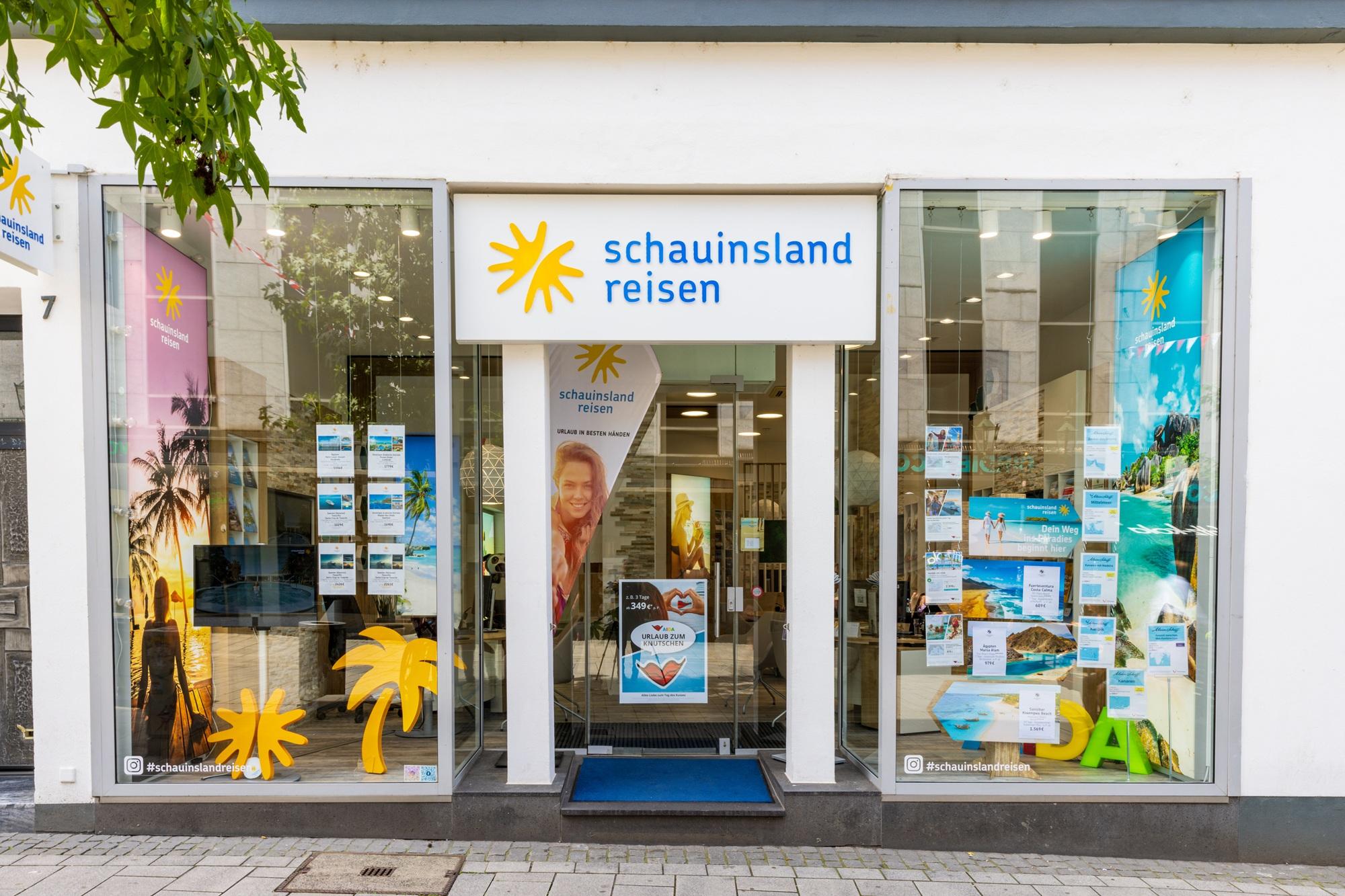 Reisebüro mit großen Schaufenstern, hellen Farben und Urlaubsmotiven zur Ferienberatung.