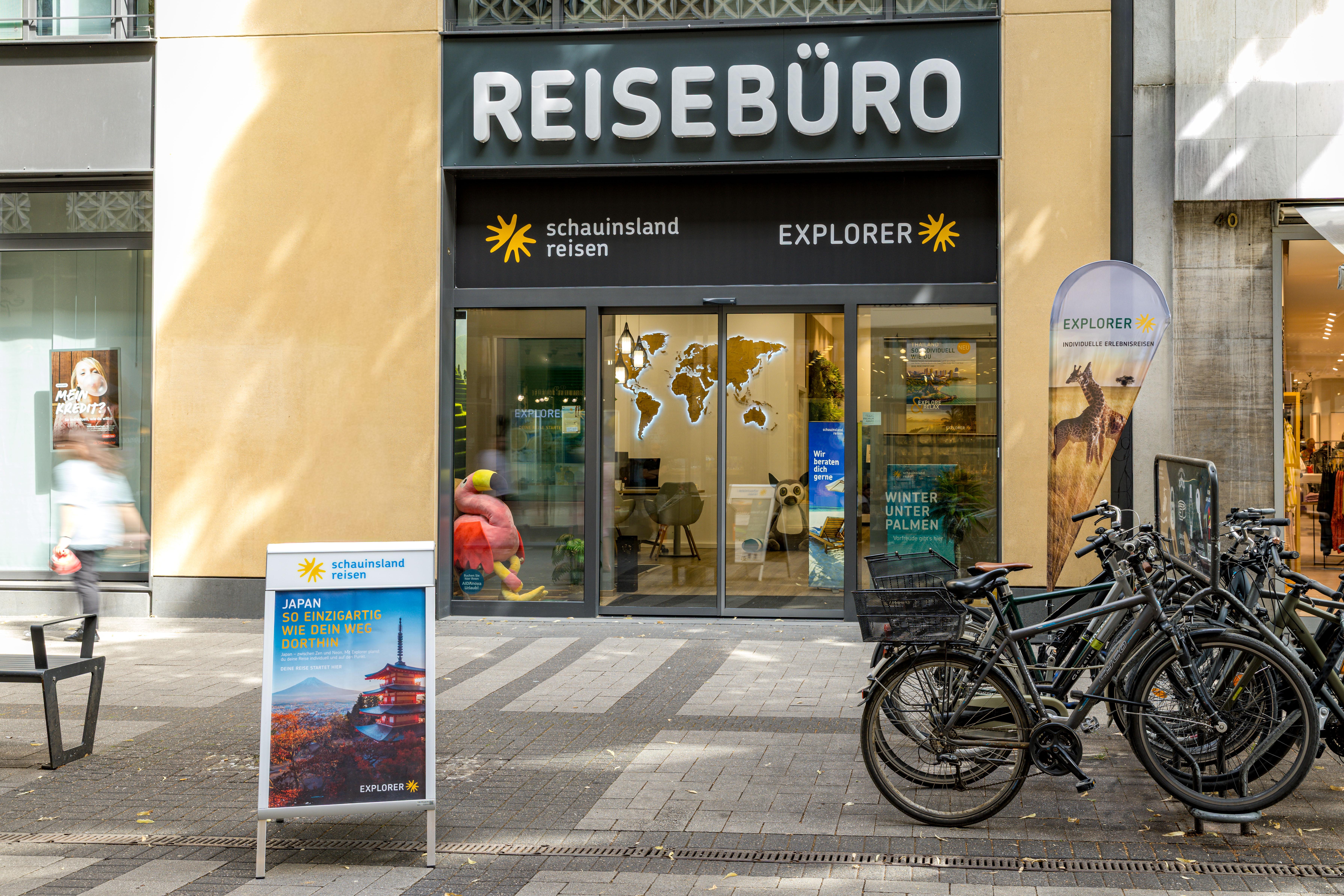 Modernes Reisebüro mit großen Fenstern und Werbung für Fernreisen in urbaner Umgebung.