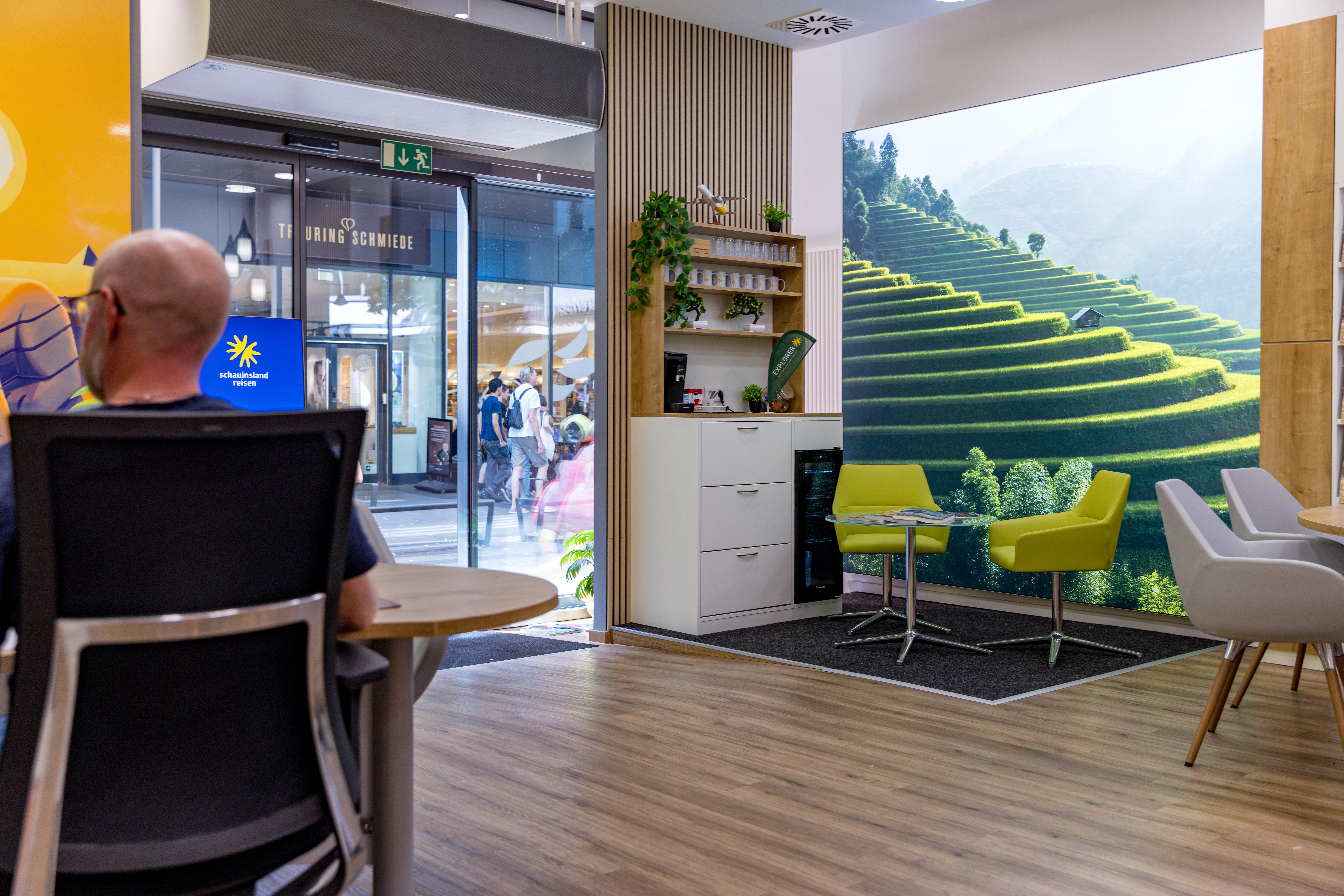 Moderner Hotellobby mit Sitzbereich und großem Wandbild von grünen, terrassierten Hügeln.