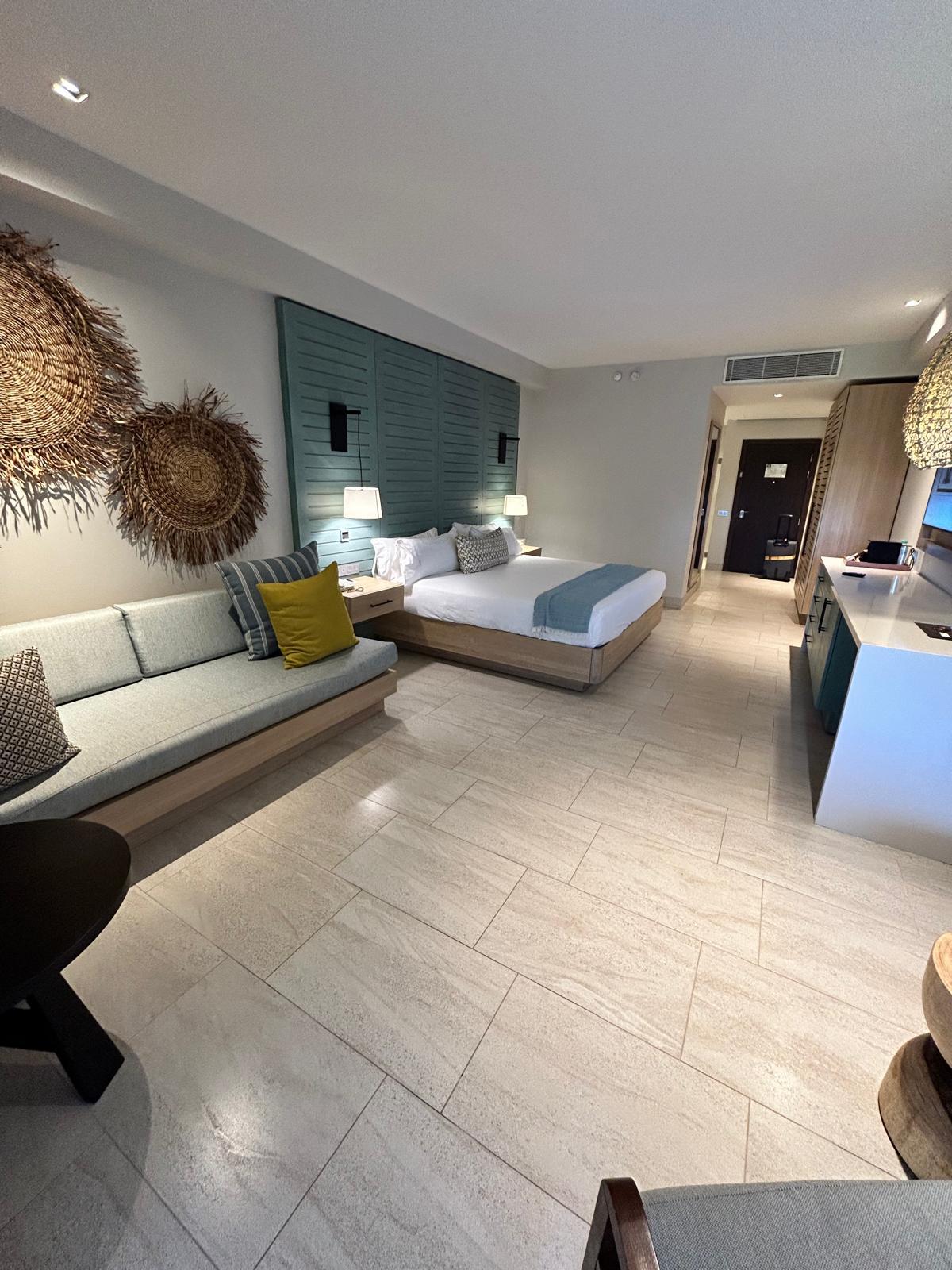 Modernes Hotelzimmer mit hellem Boden, großem Bett, Sofa und Naturdeko an der Wand.